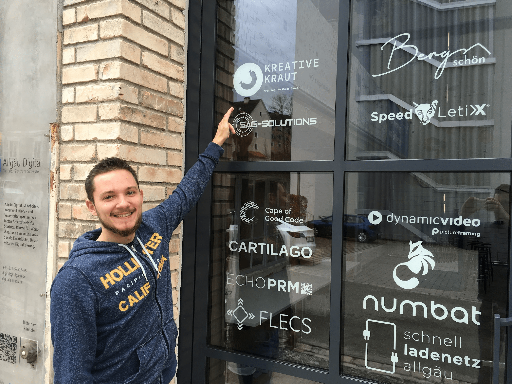 Fabi is pointing at the logo of Kreative Kraut on the door of the office door