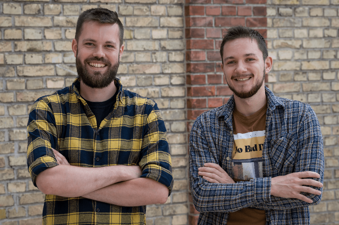 Fabi and Stefan, the founder of Kreative Kraut, are standing in front of a brick wall, smiling at the camera